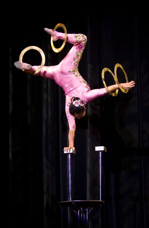 Female acrobat balancing on one hand while spinning rings on her other hand and both legs