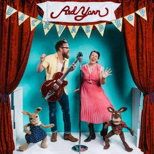 Red Yarn Photo of a man with a guitar and a woman singing into a microphone