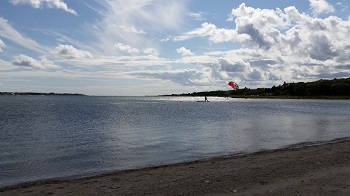 Photo of the seashore looking out to a person paragliding on the ocean