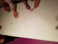 Photo of several children's hands drawing with crayons on a large piece of paper