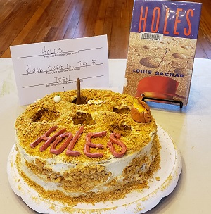 Photo of a cake with the word holes on it and the book Holes by Louis Sachar