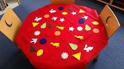 Photo of a child's table covered with a piece of red felt and multicolored felt shapes