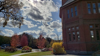 Photo of a brick library building against a blue sky with sun and clouds