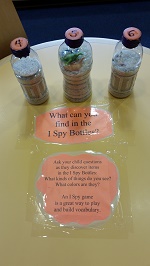 Photo of three plastic bottles on a table and a sign that says what can you find in the i spy bottles