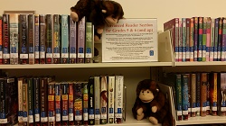 Photo of two monkey puppets looking at books on a library bookshelf
