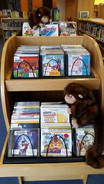 Photo of a monkey puppet sitting on a shelf of children's music cds