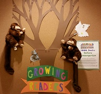 Photo of two monkey puppets in front a bulletin board with a paper tree on it