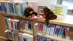 Photo of two monkey puppets looking at cd book kits on a library shelf
