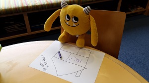 Photo of a yellow stuffed animal monster and a piece of paper and a crayon