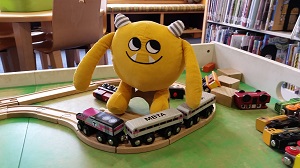 Photo of a yellow stuffed animal monster on a child's wooden train table