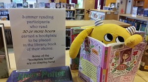 Photo of a yellow stuffed animal monster reading a book