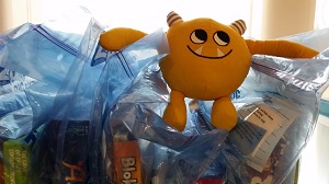 Photo of a yellow stuffed animal monster sitting on plastic bags with board games in them