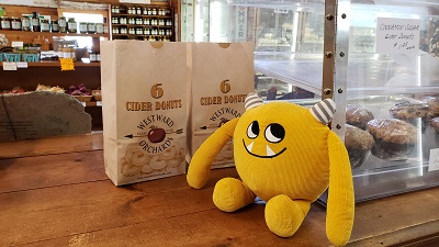 Yellow stuffed monster in store by bag of cider donuts