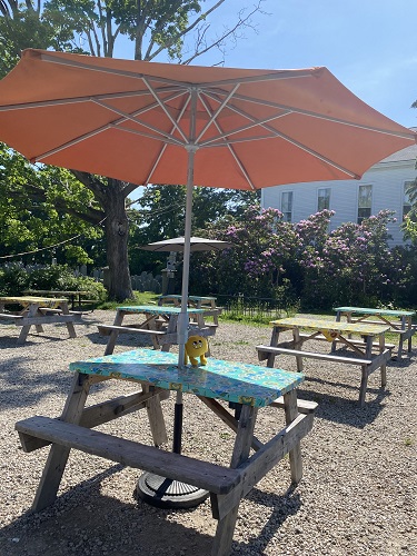 Nibbles the yellow book monster sitting on an outdoor picnic table with a blue tablecloth and orange umbrella.