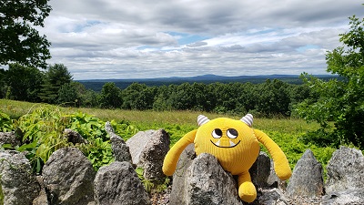 Yellow stuffed monster on stone wall by green fields