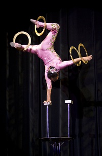Photo of an acrobat standing on one hand and spinning rings on her feet and other hand