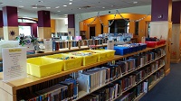 Photo of yellow blue and red plastic tubs lined up on top of a library bookshelf