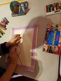 Photo of a piece of paper and a child's hands drawing on the paper