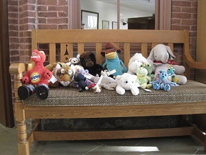 Photo of several stuffed animals sitting on a large indoor bench