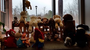 Photo of a lot of stuffed animals lined up on a bench looking out a window