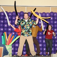 Photo of a man holding balloons in front of a wall of purple balloons
