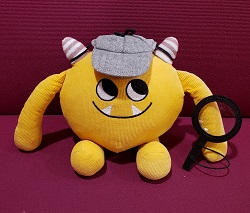 Nibbles in a Detective Hat Photo of a yellow stuffed animal monster wearing a detective hat