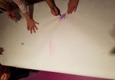 Photo of several children's hands drawing with crayons on a large piece of paper