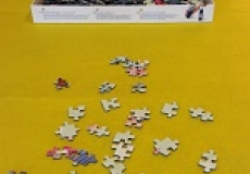 Photo of a few jigsaw puzzle pieces on a yellow piece of felt with the puzzle box in the background