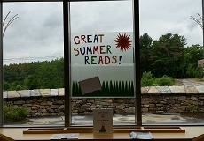 Photo looking out the children's room window onto the patio and a sign that says great summer reads