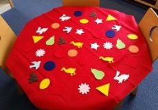 Photo of a child's table covered with a piece of red felt and multicolored felt shapes