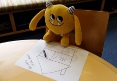 Nibbles Coloring Photo of a yellow stuffed animal monster and a piece of paper and a crayon