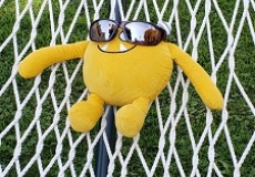 Photo of a yellow stuffed animal monster wearing sunglasses and lying in a hammock