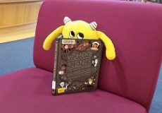 Nibbles on the Purple Chairs Photo of a yellow stuffed animal monster sitting on a purple chair reading a book