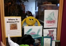Photo of a yellow stuffed animal monster sitting in the window to an office