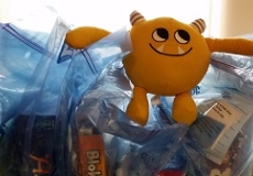 Photo of a yellow stuffed animal monster sitting on plastic bags with board games in them