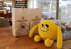 Yellow stuffed monster in store by bag of cider donuts