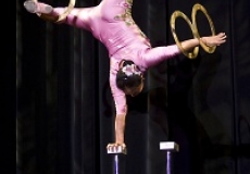 Photo of an acrobat balancing on one hand and spinning rings on her feet and other hand