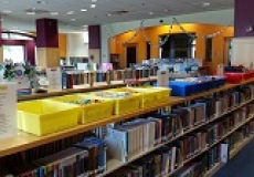Photo of plastic tubs in yellow blue and red on top of a library bookshelf