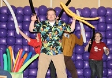 Photo of a man holding balloons in front of a wall of purple balloons