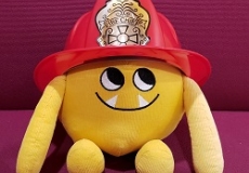 Photo of a yellow stuffed animal monster in a firefighter's helmet