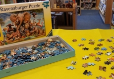 Photo of jigsaw puzzles pieces on yellow felt next to the puzzle box